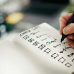 Dłoń odhaczająca punkty na odręcznej checkliście w notesie – checklista przed uruchomieniem produkcji seryjnej