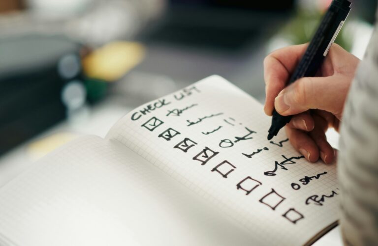 Dłoń odhaczająca punkty na odręcznej checkliście w notesie – checklista przed uruchomieniem produkcji seryjnej